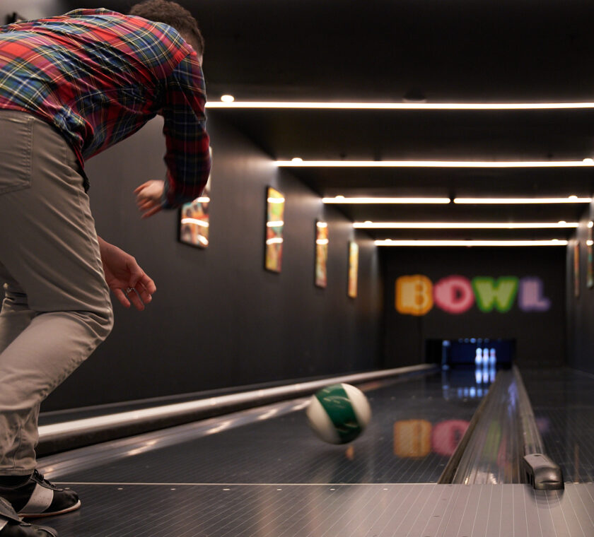 A man releases the ball down the bowling alley lane. The ball is in motion headed towards to the pins.